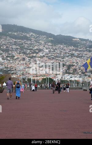Nebel; Leute, die am Hafen entlang laufen und die Stadt Funchal im Hintergrund Stockfoto