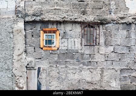 Betonziegelwand und kleine Fenster eines verlassenen alten Gebäudes außen. Stockfoto