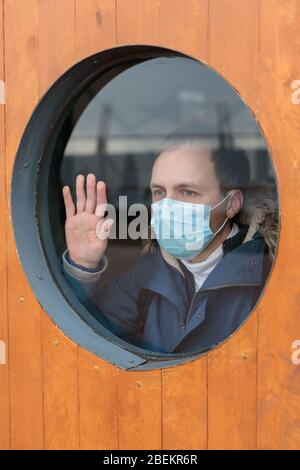 Der Mensch schaut hinaus und berührt das Fenster, trägt eine medizinische Schutzmaske gegen übertragbare Infektionskrankheiten und als Schutz gegen Grippe, Coronavirus, Stockfoto