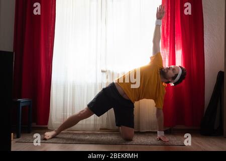 Fröhlicher Mann, der eine seitliche Plank-Übung im Zimmer macht Stockfoto