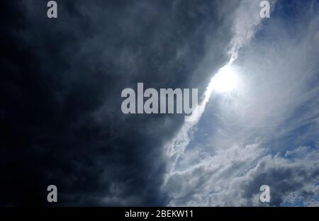 Sonnenschein hinter dunklen Wolken am blauen Himmel Stockfoto