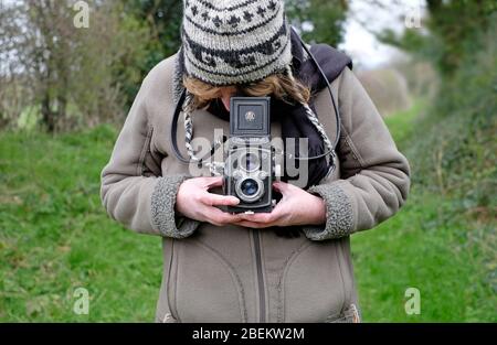 Ältere weibliche Person mit Vintage-Spiegelreflexkamera auf dem Land Stockfoto