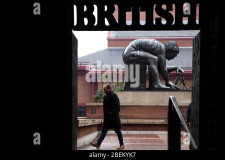 Ein Mann, der über den Innenhof der British Library mit der Skulptur "Newton" von Eduardo Paolozzi im Hintergrund geht, London Stockfoto