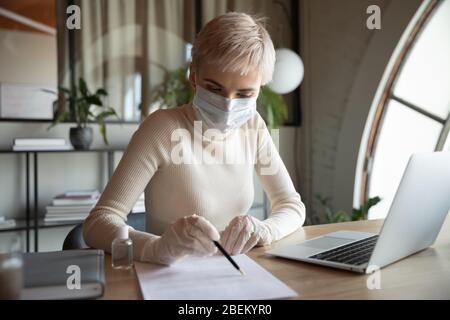 Weibliche Mitarbeiterin in Schutzmaske und Handschuhen, die arbeitet Stockfoto