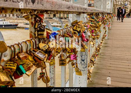 Nahaufnahme von Vorhängeschlössern aus Liebe auf der Debilly-Fußgängerbrücke, mit einem jungen Paar dahinter, in Paris, Frankreich. Februar 2020. Stockfoto