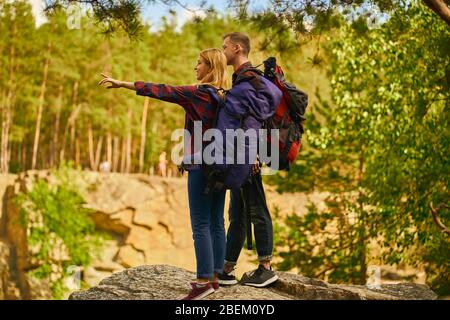 Nettes Paar mit Rucksäcken stehen am Felsen in der Nähe des Sees im Wald und Canyon Hintergrund. Reisekonzept. Tourismuskonzept. Stockfoto