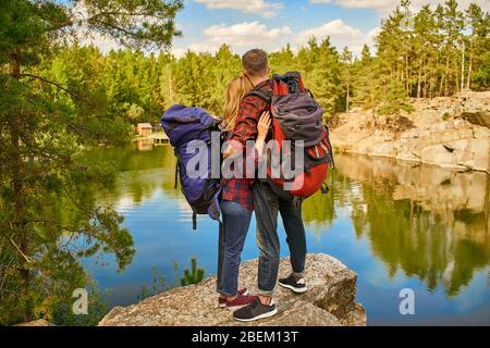Nettes Paar mit Rucksäcken stehen am Felsen in der Nähe des Sees im Wald und Canyon Hintergrund. Reisekonzept. Tourismuskonzept. Stockfoto