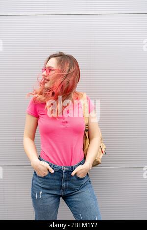 Schöne Frau mit rosa gefärbten Haaren und Neon-Sonnenbrille über der grauen Wand stehen. Fliegende Frisur Stockfoto