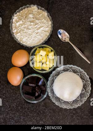 Zutaten für eine Torte, darunter Mehl, Butter, Eier, Schokolade und Zucker auf dunklem Hintergrund Stockfoto