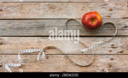 Roter Apfel mit Maßband auf Holzhintergrund. Maßband bildet das Herzkonzept Ernährung Harmonie und gesundes Leben Stockfoto