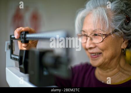 Ältere Frau, die sich auf Waagen wiegt Stockfoto