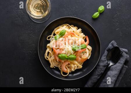 Italienische Pasta Fettuccine mit Garnelen und einem Glas Weißwein auf schwarzem Tisch. Stockfoto