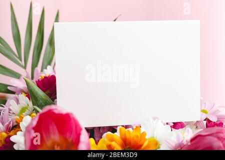 Blumen verspotten Glückwünsche. Glückwunschkarte in Blumenstrauß auf rosa Hintergrund. Weiße leere Karte mit Platz für Text, Frame Mockup Stockfoto