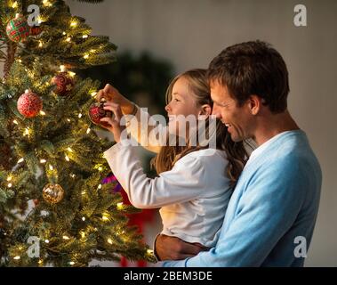 Glücklicher Vater und Tochter schmücken einen Weihnachtsbaum zusammen Stockfoto