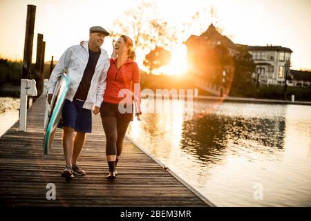 Ein reifes Paar, das auf einem See Pier mit einem Paddelbrett läuft Stockfoto