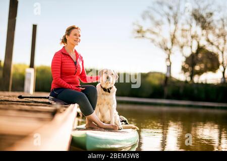 Frau mit mittlerem Erwachsenen, die mit ihrem Haustier auf einem Dock sitzt Stockfoto