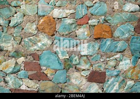 Hintergrund mit türkisfarbenen und braunen Steinen. Wand aus blauen und burgunderroten groben Steinen. Stockfoto