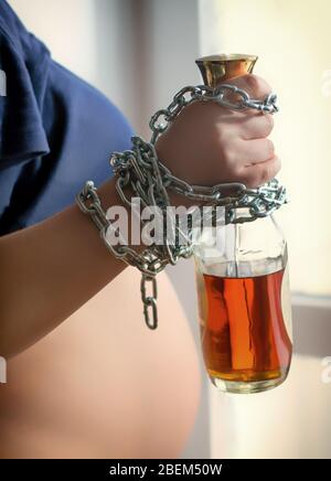 Hand einer schwangeren Frau, die mit einer Flasche Alkohol verkettet ist Stockfoto