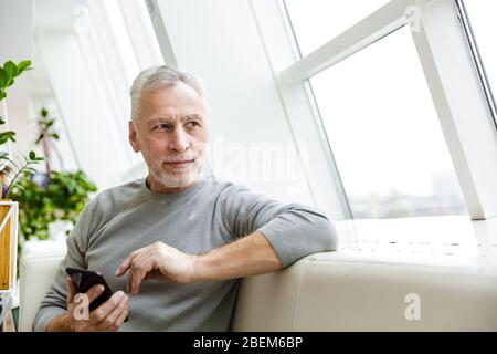 Bild eines älteren grauhaarigen bärtigen Geschäftsmannes sitzen im Café mit Handy zur Seite schauen. Stockfoto