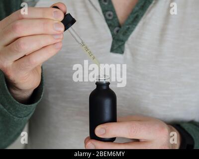 Eine Flasche und eine Pipette mit CBD- und THC-Tinktur-Lösung wird aus der Nähe gezeigt und von einem Paar männlicher Hände gehalten. Stockfoto