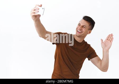 Porträt von freundlichen schönen kaukasischen Mann Video-Chat mit Freunden während covid19 Selbstquarantäne, sagen hallo zu Anhängern als Selfie oder Stockfoto