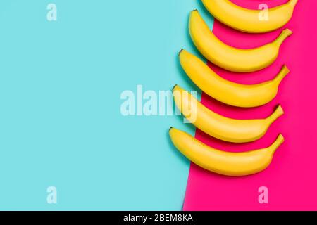 Nahaufnahme von reifen gelben Bananen auf einem bunten rosa und blauen Hintergrund. Draufsicht Stockfoto