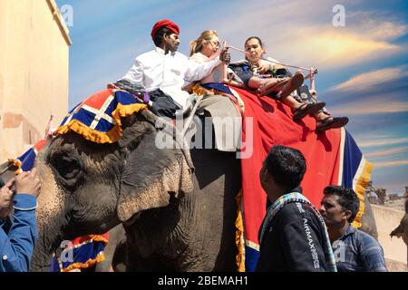 Schuss einer mit rotem Tuch bedeckten Elefantenlinie mit Touristen, die auf ihnen zum Wahrzeichen der Bernsteinhügelland in Jaipur fahren Stockfoto