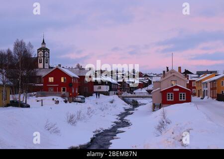 Die historische Bergbaustadt Røros mit der Kirche Bergstadens Ziir und dem zugefrorenen Fluss Hyttelva im Winter, Norwegen. Stockfoto