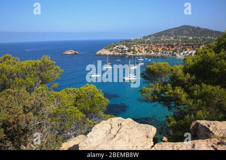 Blick von der Südküste Ibizas mit Booten, die in der Bucht verankert sind. Schöne Landschaft mit Klippen & türkisfarbenem Wasser. Baleric-Inseln, Spanien. Stockfoto