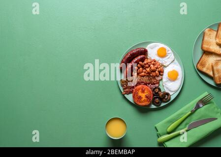 Englisches Frühstück mit Würstchen, Bohnen, Pilzen und Eiern auf einem grünen Tisch. Flaches Lay mit britischem kompletten Frühstücksteller. Traditionelle englische Küche. Stockfoto