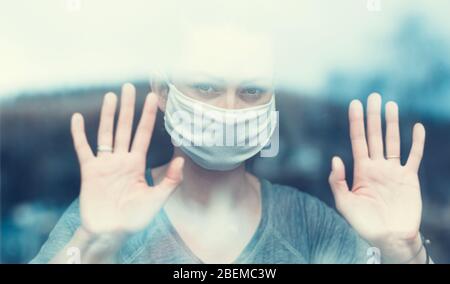 Frau steht an einem Fenster in einer Schutzmaske - Konzept des Aufenthalts zu Hause - Home Quarantäne - Coronavirus Pandemie in der Welt - flache Tiefe Stockfoto