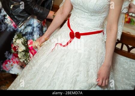 Braut in weißem Kleid mit rotem Band. Band auf dem Bauch der Braut. Stockfoto