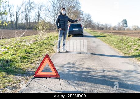 Rotes Warndreieck auf der Straße vor einem zerbrochenen Auto. Der junge Mann sucht Hilfe beim Anhalten von Fahrzeugen, die sich bewegen Stockfoto