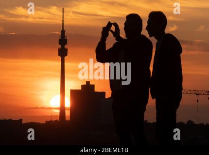 Dortmund, Deutschland. April 2020. Zwei junge Männer fotografieren bei Sonnenuntergang auf der Schlammhappe am Phoenix Lake. Im Hintergrund der Fernsehturm 'Florian', eines der Wahrzeichen der Stadt. Um das Corona-Virus einzudämmen, hat NRW alle Ansammlungen von drei oder mehr Menschen in der Öffentlichkeit verboten. Quelle: Bernd Thissen/dpa/Alamy Live News Stockfoto