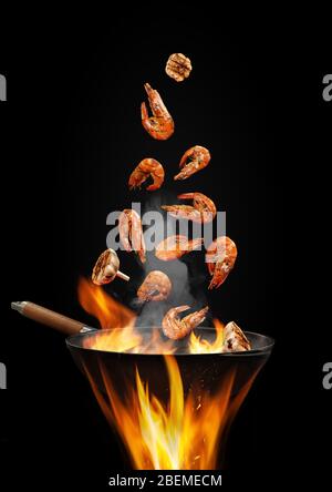 Wok Pfanne mit Rauch über Feuer braten einige Garnelen mit Knoblauch vor schwarzem Studio Hintergrund. Kochkonzept. Nahaufnahme Stockfoto