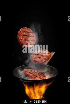 Wok Pfanne mit Rauch über Feuer ist Braten drei Rindfleisch Schnitzel vor schwarzem Studio Hintergrund. Kochkonzept. Nahaufnahme Stockfoto