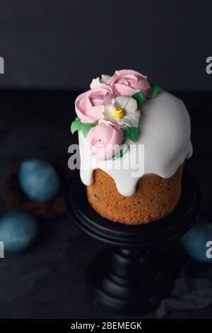 Osterkuchen mit rosa cremigen Rosen auf schwarzem Holzständer auf dunkelgrauem texturiertem Hintergrund. Urlaubskonzept. Inspiration für Ostern. Kopierbereich Stockfoto