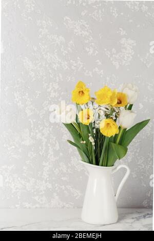 Bouquet von schönen gelben Narzissen und weißen Tulpen in Vase auf Marmortisch. Frühling Stillleben Konzept Stockfoto