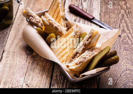 Hausgemachte Thunfisch-Sandwiches mit Käse serviert mit Gurken auf rustikalem Holztisch Stockfoto