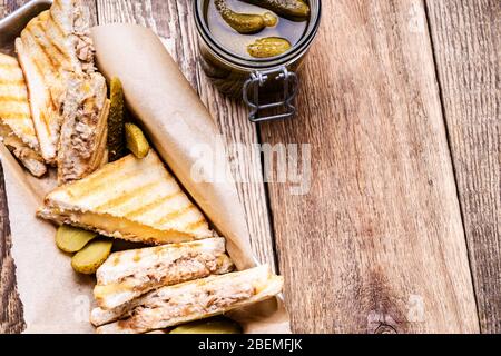 Hausgemachte Thunfisch-Sandwiches mit Käse serviert mit Gurken auf rustikalem Holztisch Stockfoto