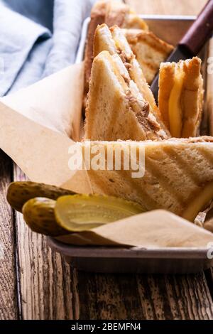 Hausgemachte Thunfisch-Sandwiches mit Käse serviert mit Gurken auf rustikalem Holztisch Stockfoto