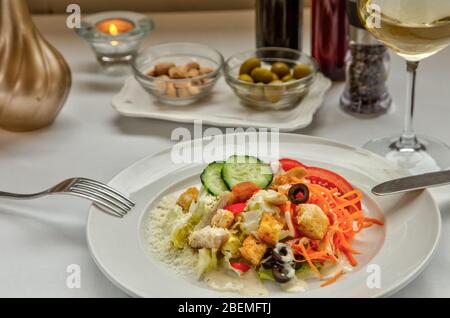 Köstlicher frischer Caesar-Salat mit Croutons, Speck, Salat, Gemüse, Parmesan und Mayonnaise. Rosetten mit Mandeln und grünen Oliven und ein Glas Stockfoto