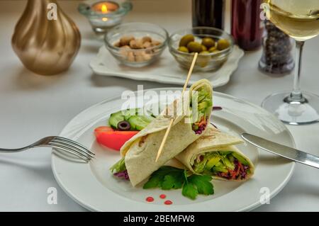 Gemüserollen. Pfannkuchen mit Gemüse. Pita Brot in Kohl, Gurke, Avocado, Karotten, Kohl, Salat verpackt. Das Gericht ist mit Zwiebeln dekoriert Stockfoto