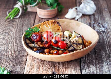 Vegane pflanzliche Gericht, Schüssel mit Quinoa, Kichererbsen, gegrillte Zucchini, Auberginen, Tomaten in Keramikschale auf rustikalem Holztisch, nachhaltig lebensrettend Stockfoto