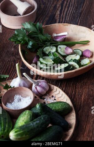 Veganes Gericht auf pflanzlicher Basis, frischer Salat mit Bio-Gemüse und Kräutern, Gurken, Petersilie und Knoblauch in Keramikschale auf rustikalem Holztisch, Stockfoto