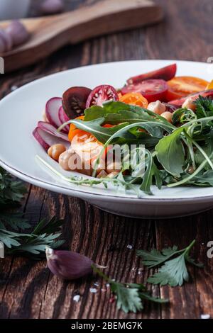 Vegane pflanzliche Gericht, Schüssel mit Kichererbsen, frische bunte Tomaten, in Scheiben geschnittenen Rettich, Gurke, Kräuter in Keramikschale auf rustikalem Holztisch, Sustainab Stockfoto