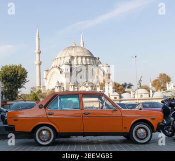 Altes klassisches orangenes Fahrzeug im Parkhaus fotografiert. Im Hintergrund befindet sich eine Moschee. Nahaufnahme. Stockfoto