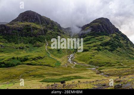 Wasser, das nach dem starken Regen von den Three Sisters of Glen Coe Coire nan Lochan mit Gearr Aonach (692M links), Guala Laidir (rechts) und Stob Coire abfließt Stockfoto