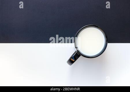 Schwarz-weiße Oberfläche mit einem schwarzen Becher mit Milch. Horizontale Linie. Abstraktes konzeptuelles Bild. Stockfoto