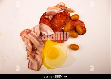 Zerbrochenes Hühnerei, Speck- und Wurstscheiben sowie Tomaten auf weißem Hintergrund. Nahaufnahme Stockfoto